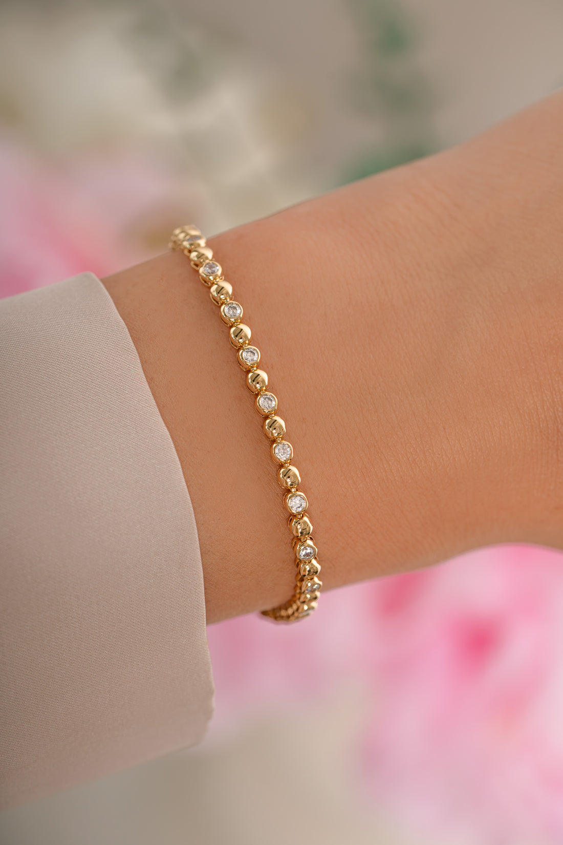 Gold bracelet on a wrist with a blurred floral background
