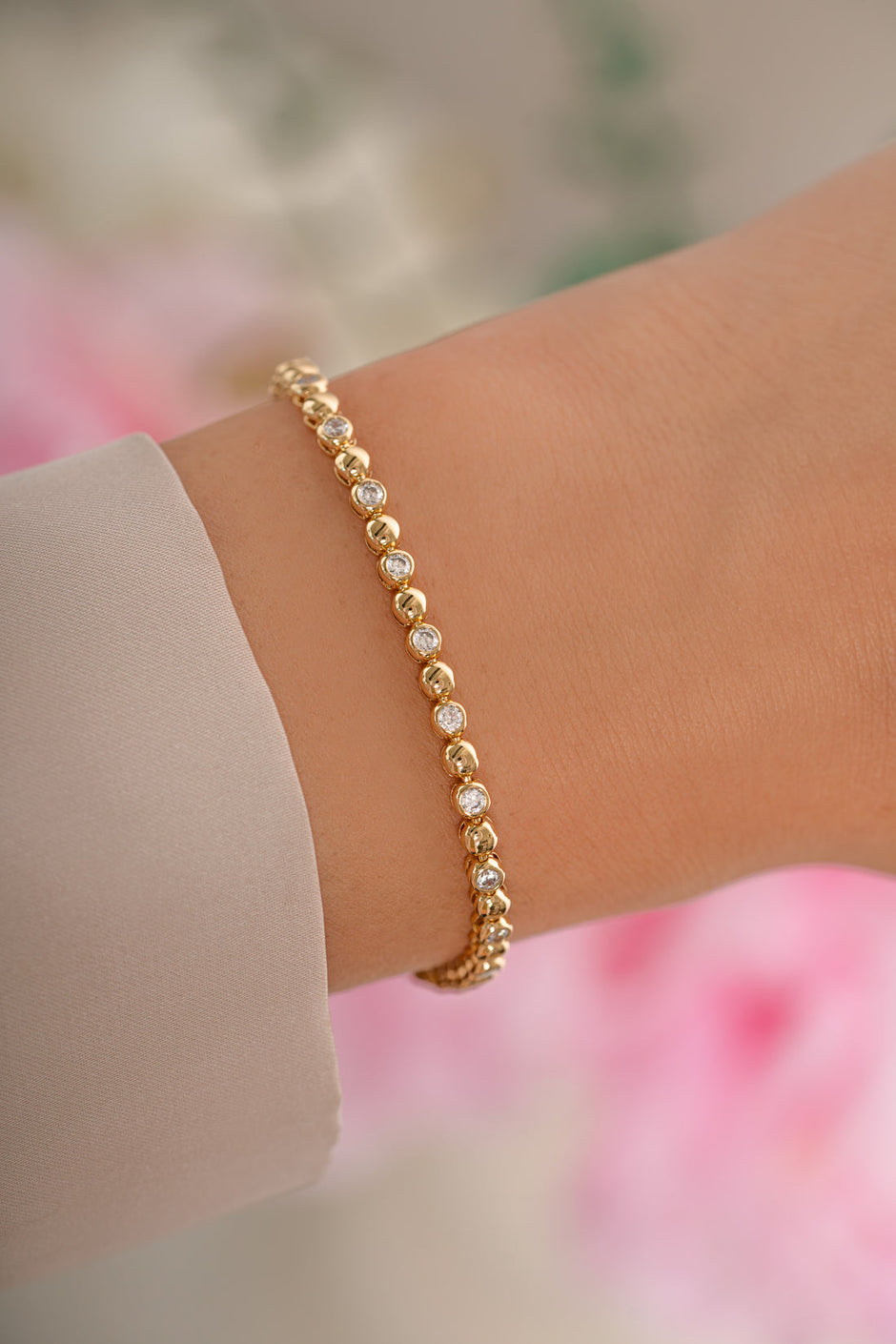 Gold bracelet on a wrist with a blurred floral background